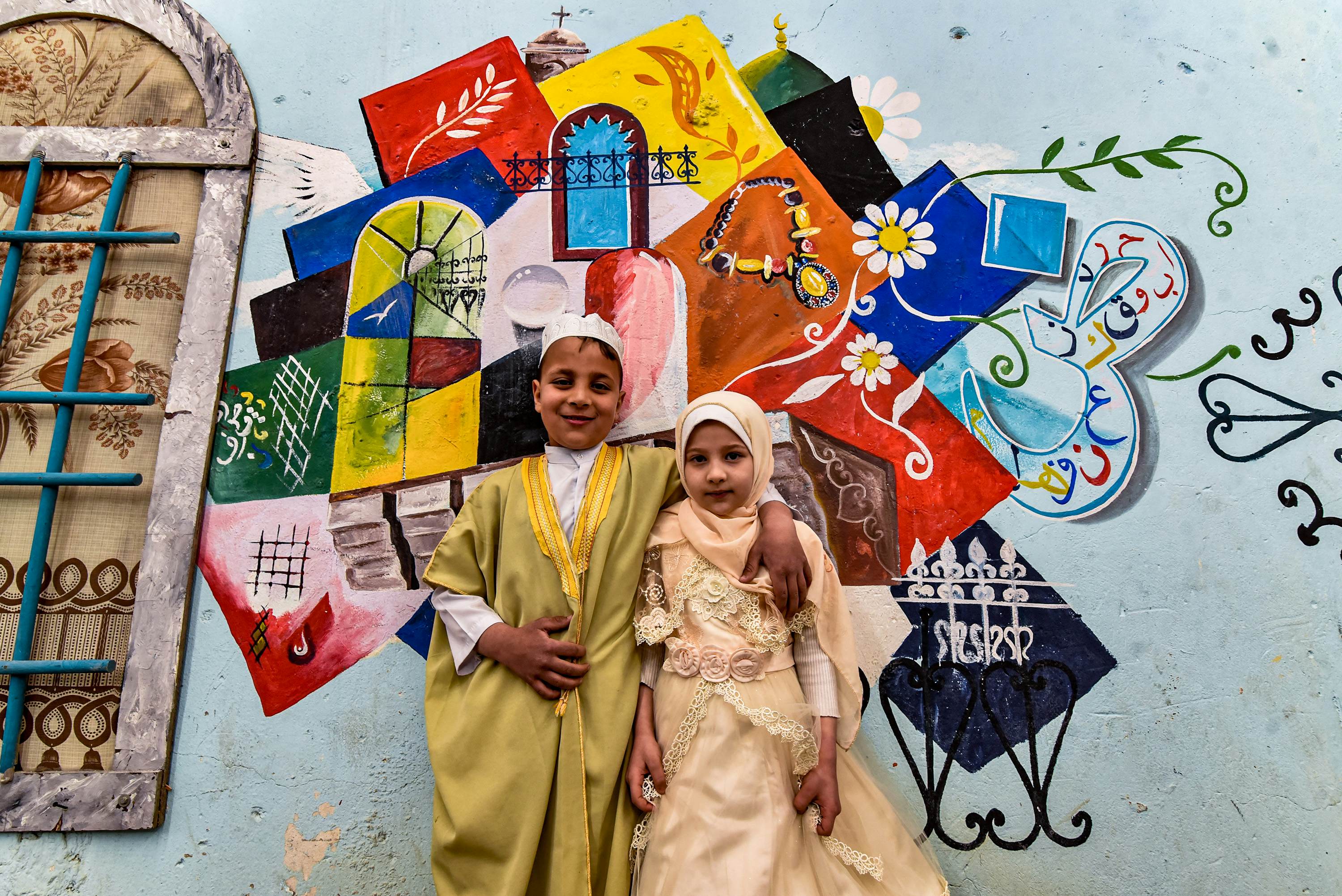 Children pose for a photo in front of a large graffiti depicting cultural elements including mosques, churches, old window lattices of the old town of Iraq's northern city of Mosul, on the first night of the Muslim holy fasting month of Ramadan on April 13, 2021, during a celebration hosted by a local cultural NGO. (Photo by Zaid AL-OBEIDI / AFP) (Photo by ZAID AL-OBEIDI/AFP via Getty Images)